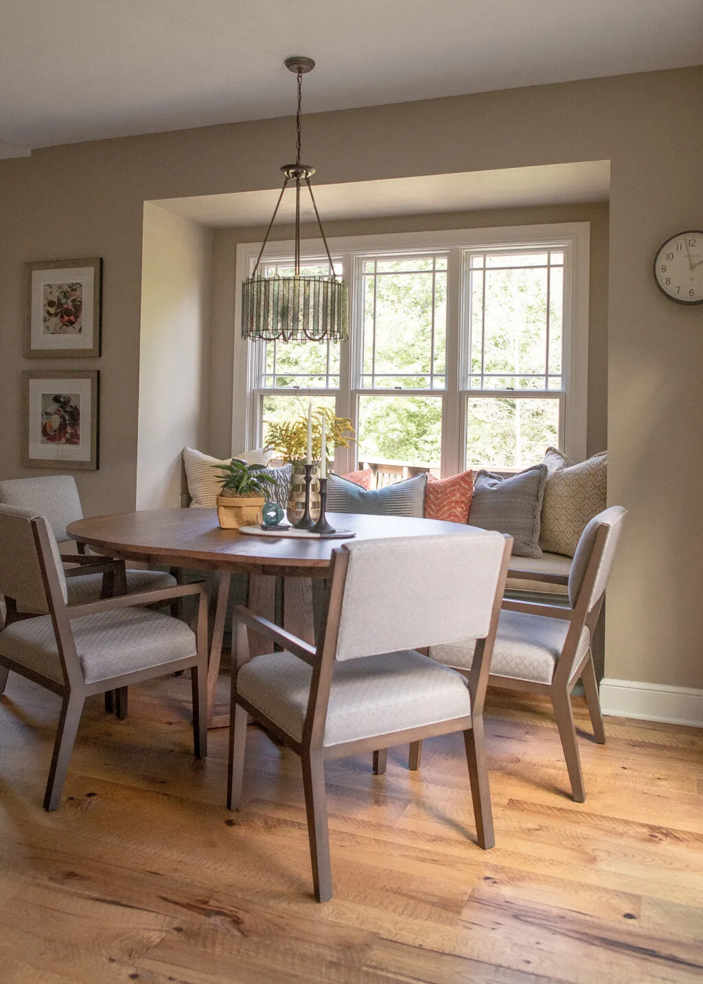 Kitchen nook with round table, modern gray/wood chairs, and window seat with orange and blue pillows