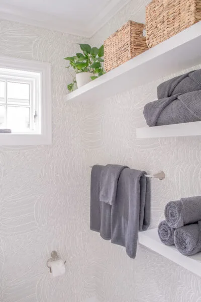 Moreland Hills home designed by Reflections Interior Design Powder room area with gray towels and greenery