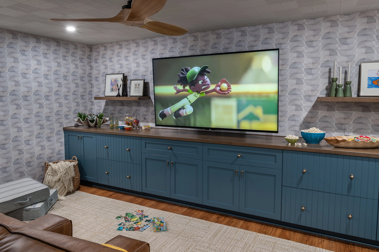 movie room with custom blue cabinetry, large tv, and patterned wallpaper