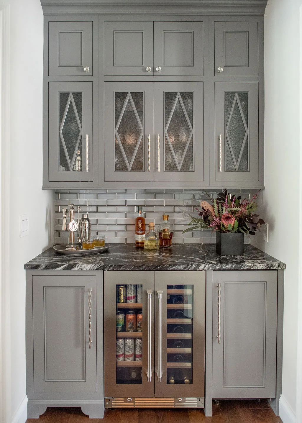 Home bar with gray cabinetry, glass paneled doors, and luxury mini fridge