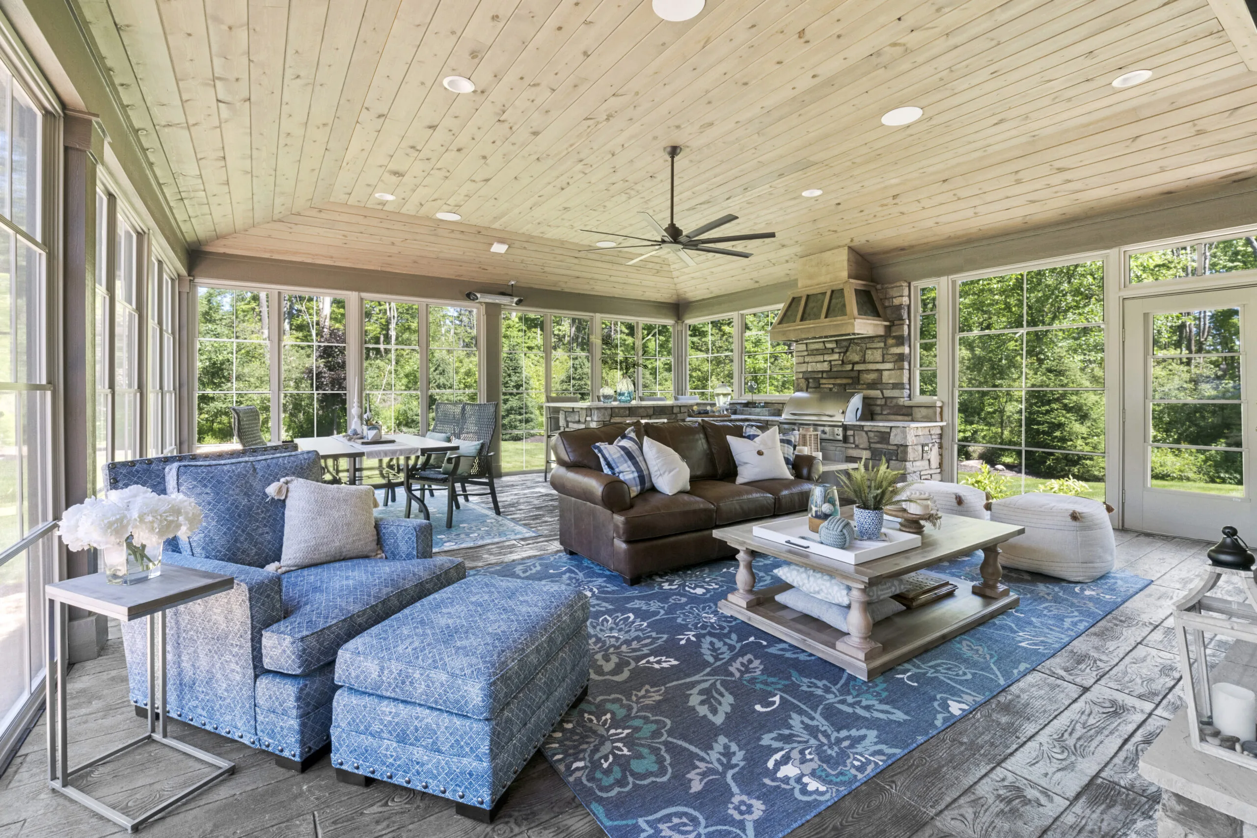 Sun room with grill area, dark leather couch, blue longe chair, and light blue rug