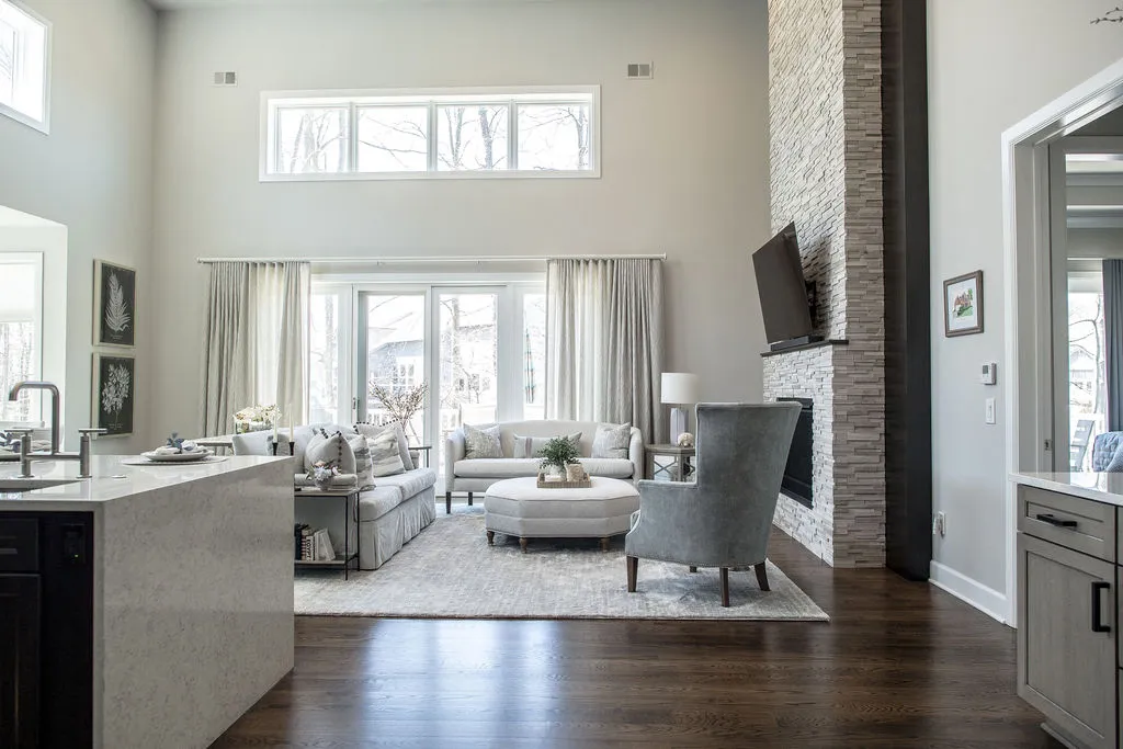 View into a living room with a stone fireplace, lounge chair, ottoman, and sofa with neutral and blue hues