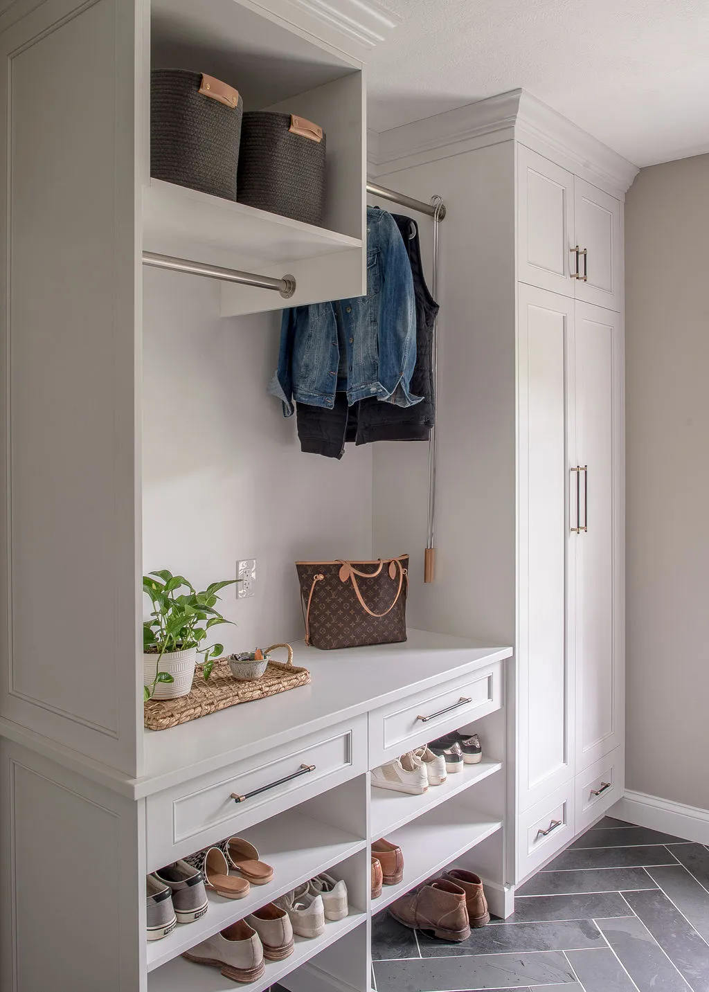 Mudroom with white cabinetry with shoe storage and dark herringbone floor tile