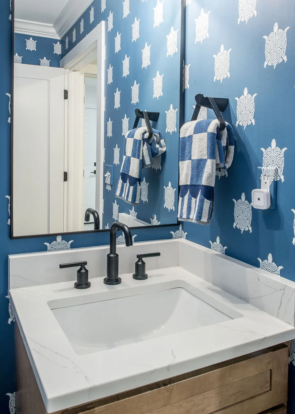 Image of a white sink with a black faucet and blue/white turtle wallpaper on the surrounding walls