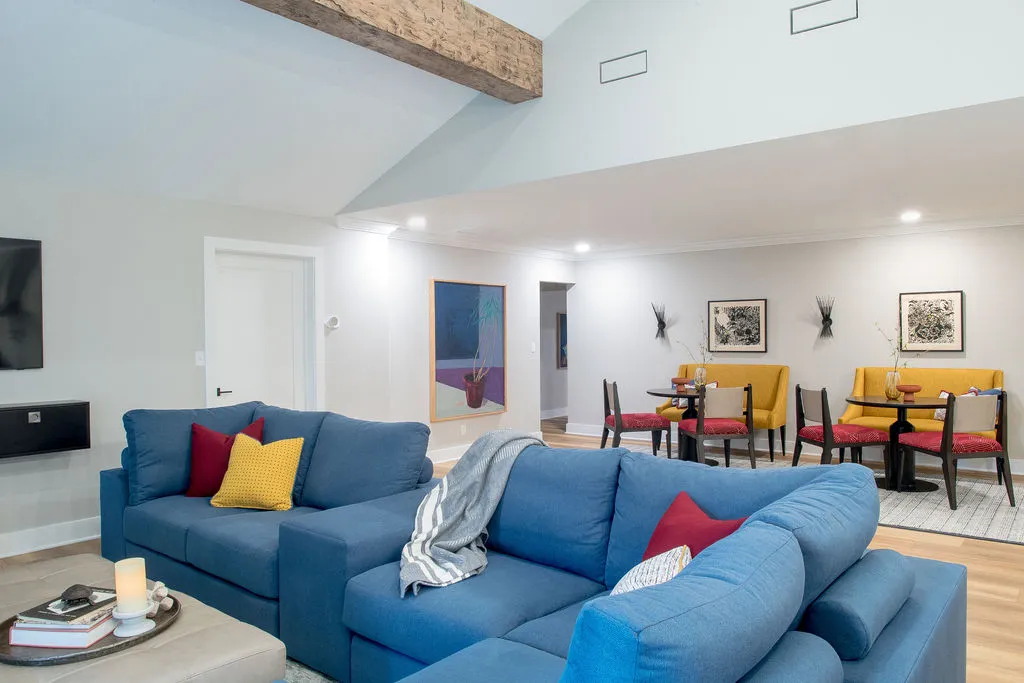 Living room with a blue sofa and red/yellow pillows, coffee table in front, and a seating area in the background