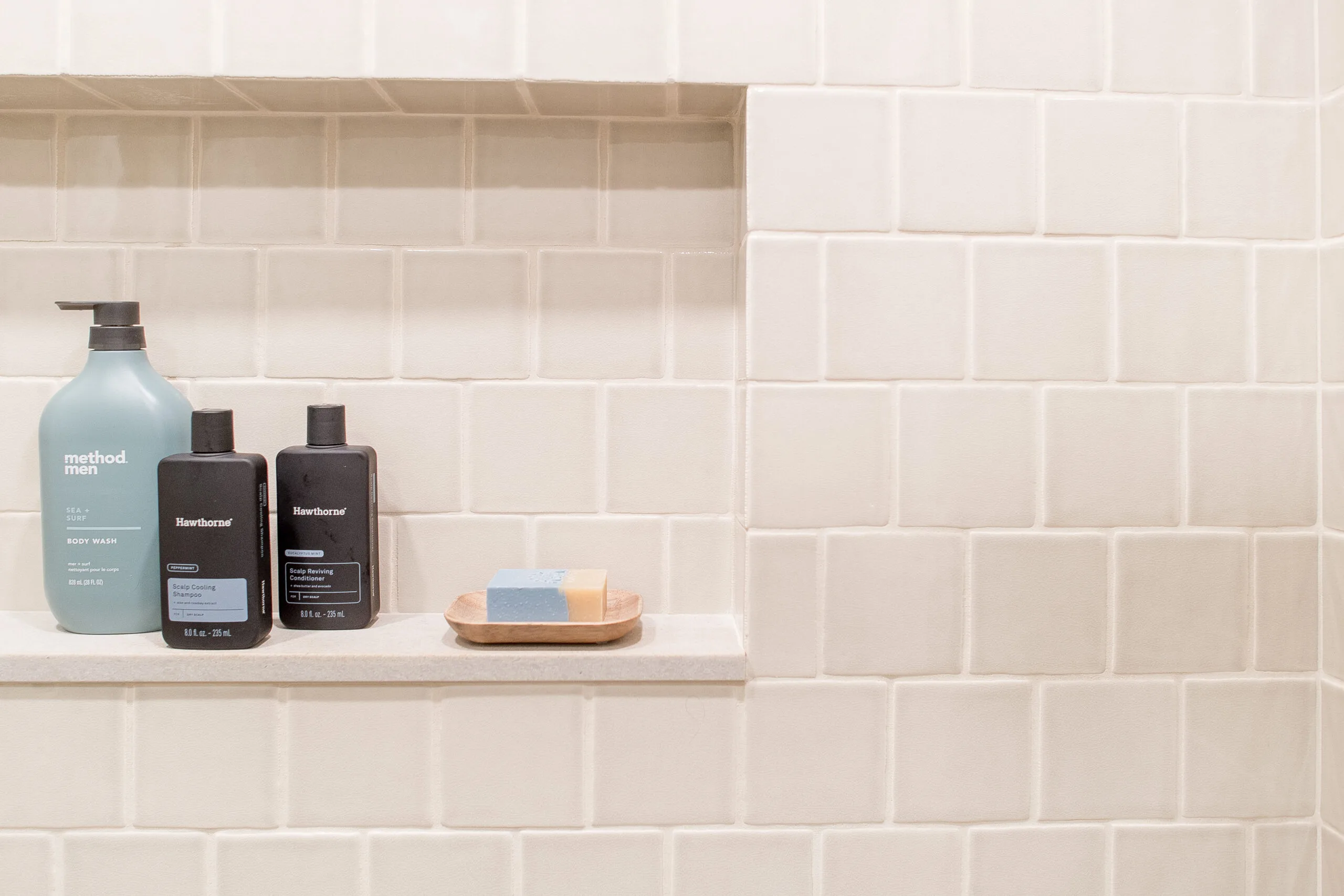 Close up of a shower niche with neutral tile with soap and shampoo/conditioner