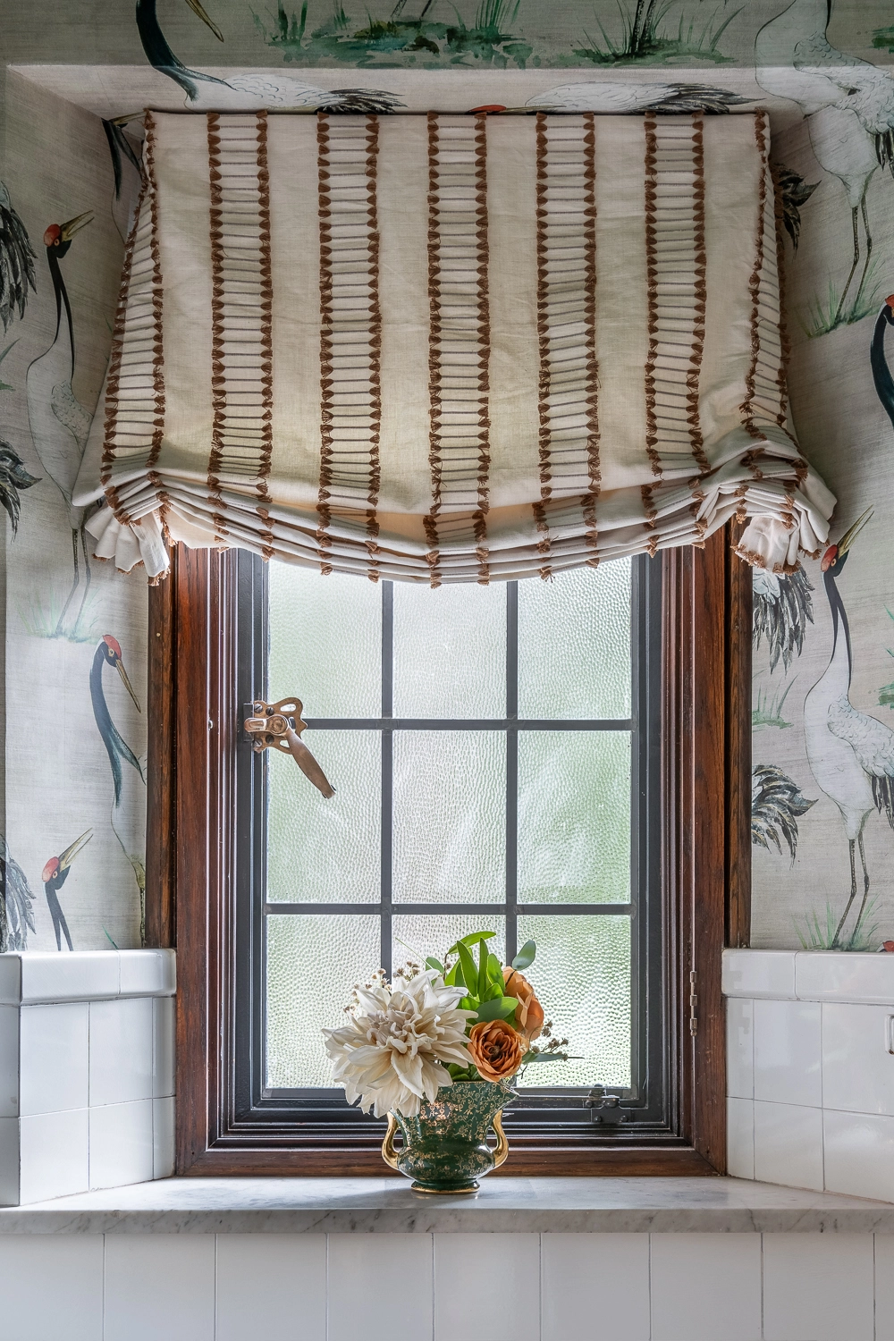 Image looking at a window of a powder room with a relaxed roman shade and florals on the windowsill